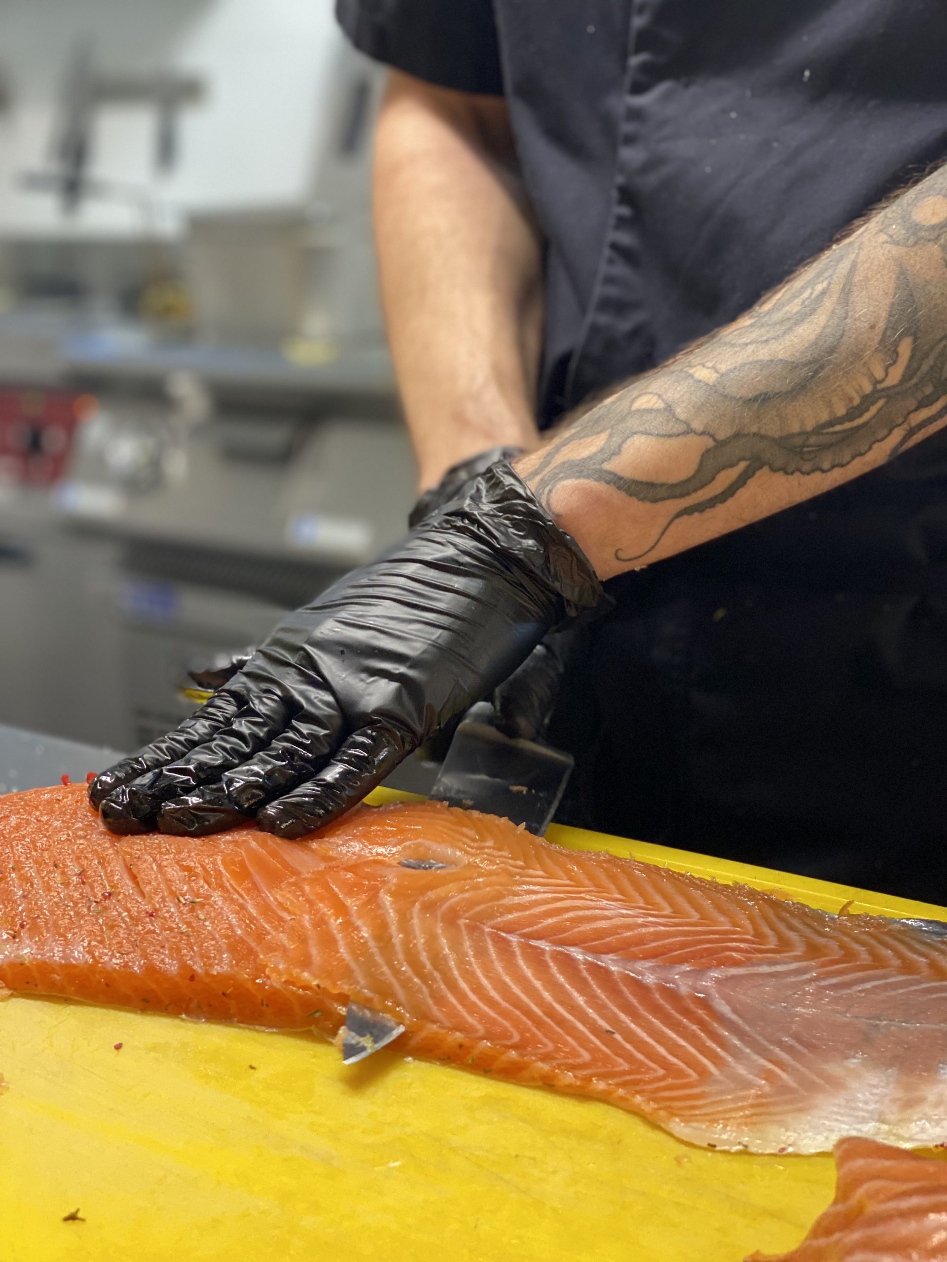 Personne portant des gants noirs et coupant un morceau de saumon à la manufacture du bâtiment